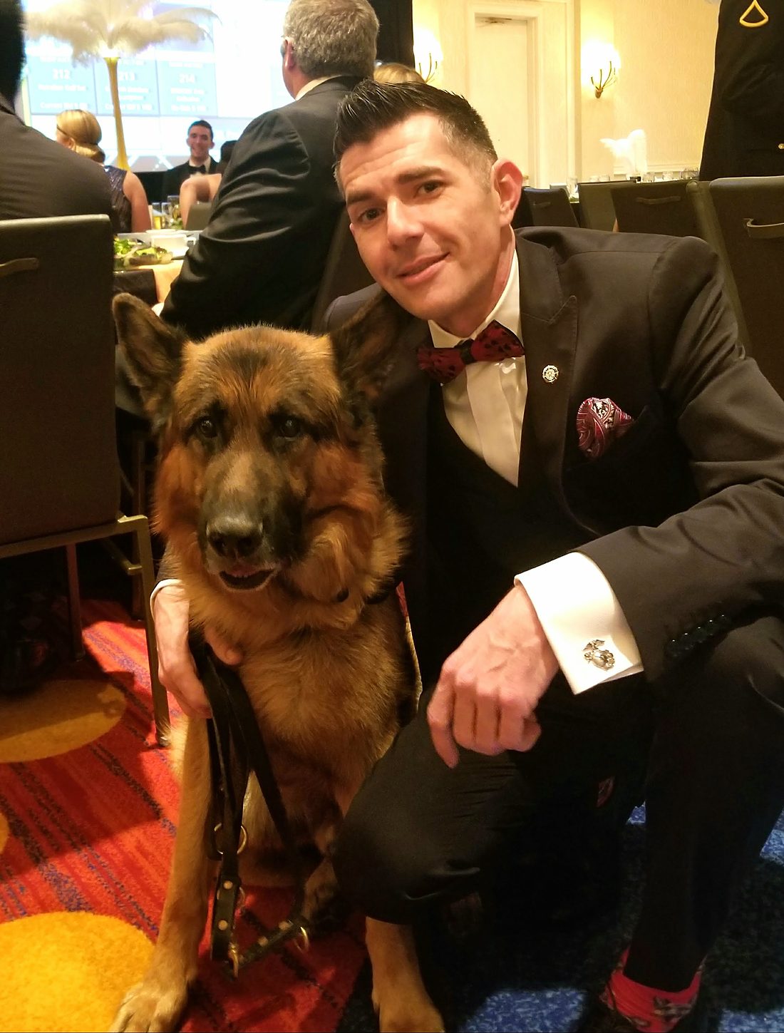Kenny Bass in formal attire kneeling beside Atlas at an event.
