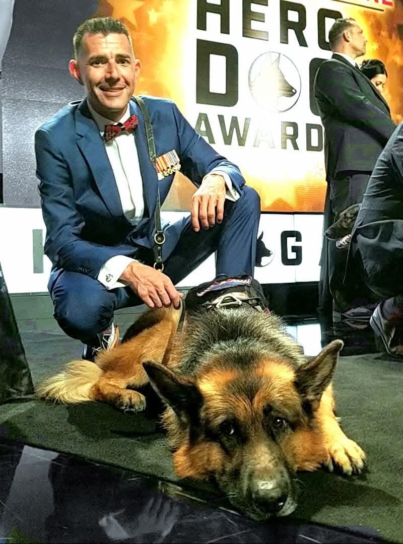 Kenny Bass kneeling beside Atlas at the 2017 American Humane Hero Dog Awards.
