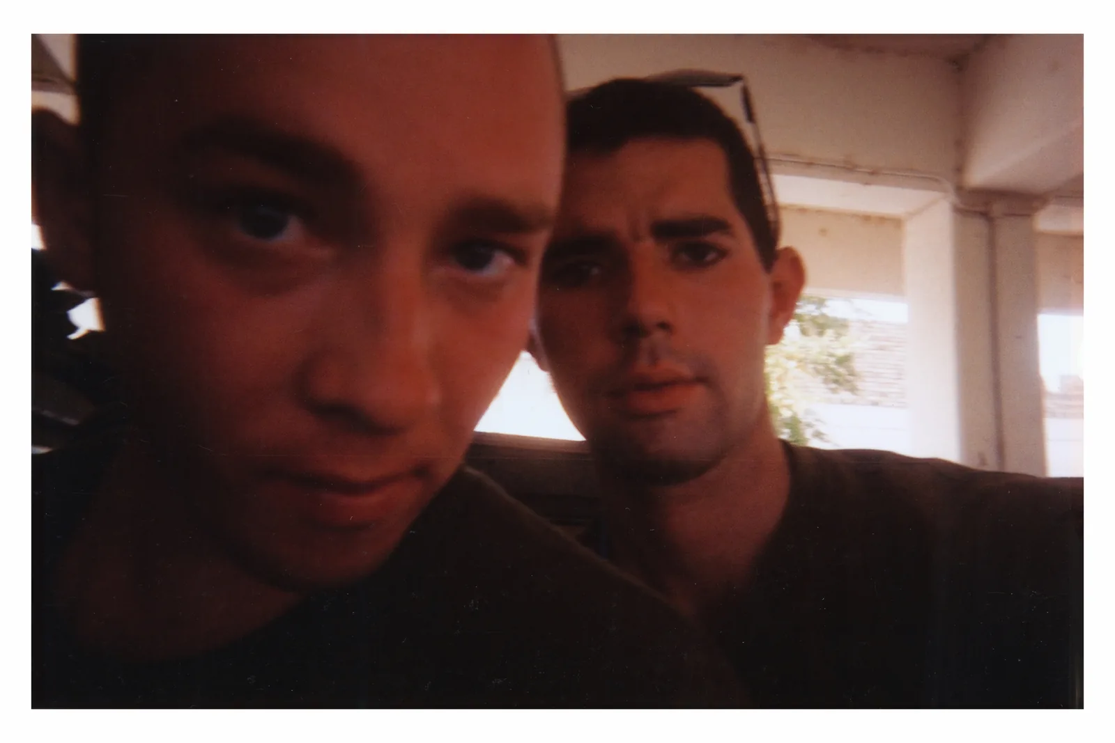 Tim Jones fills the left foreground, cropped at the forehead. Kenny Bass is farther back on the right, with sunglasses on his head, beneath a concrete canopy.