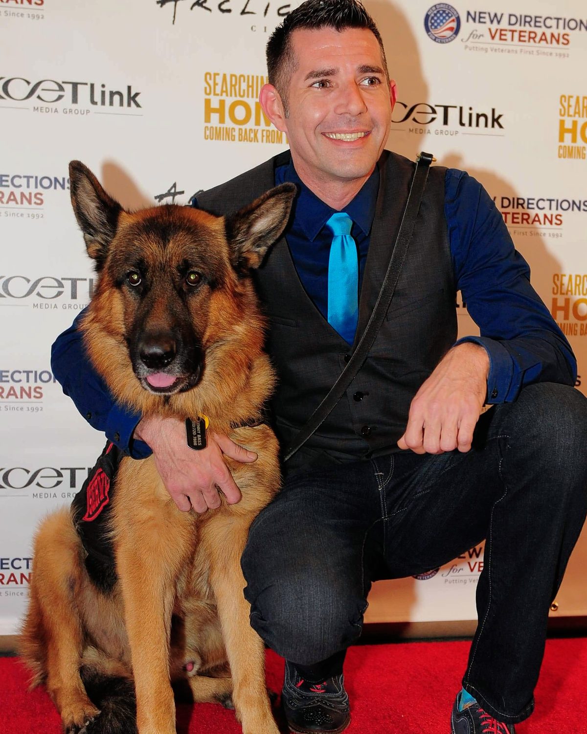 Kenny Bass kneeling beside Atlas on a red carpet in front of a Searching for Home backdrop.
