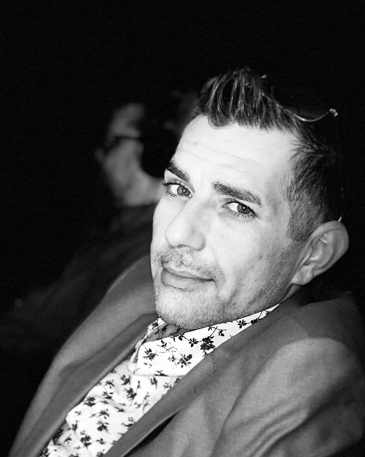 Black-and-white editorial headshot of Kenny Bass in a suit and patterned shirt.